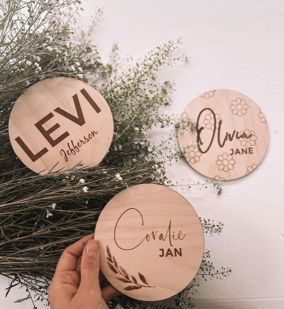 Name Announcement Discs | Double Sided w/ Birth Stats by Petit Nordique baby name wooden engraved discs next to wildflowers hand holding