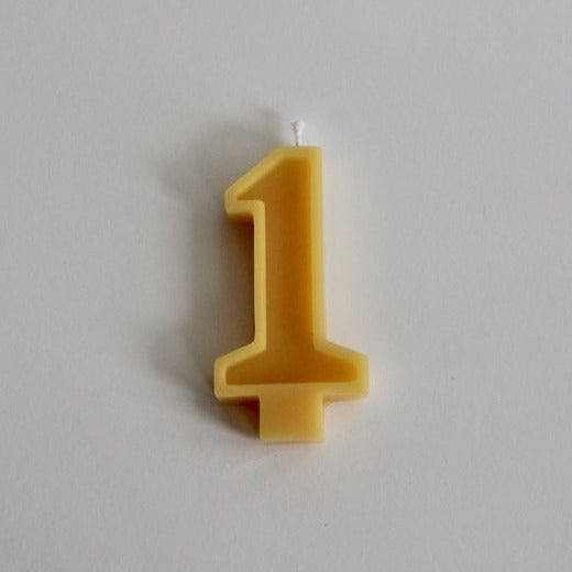 White background with 100% Pure Canadian Beeswax Candle in "1" by Fersk Self Care. Candle is a natural yellow beeswax colour, with the number  "1" and a wick on the top,