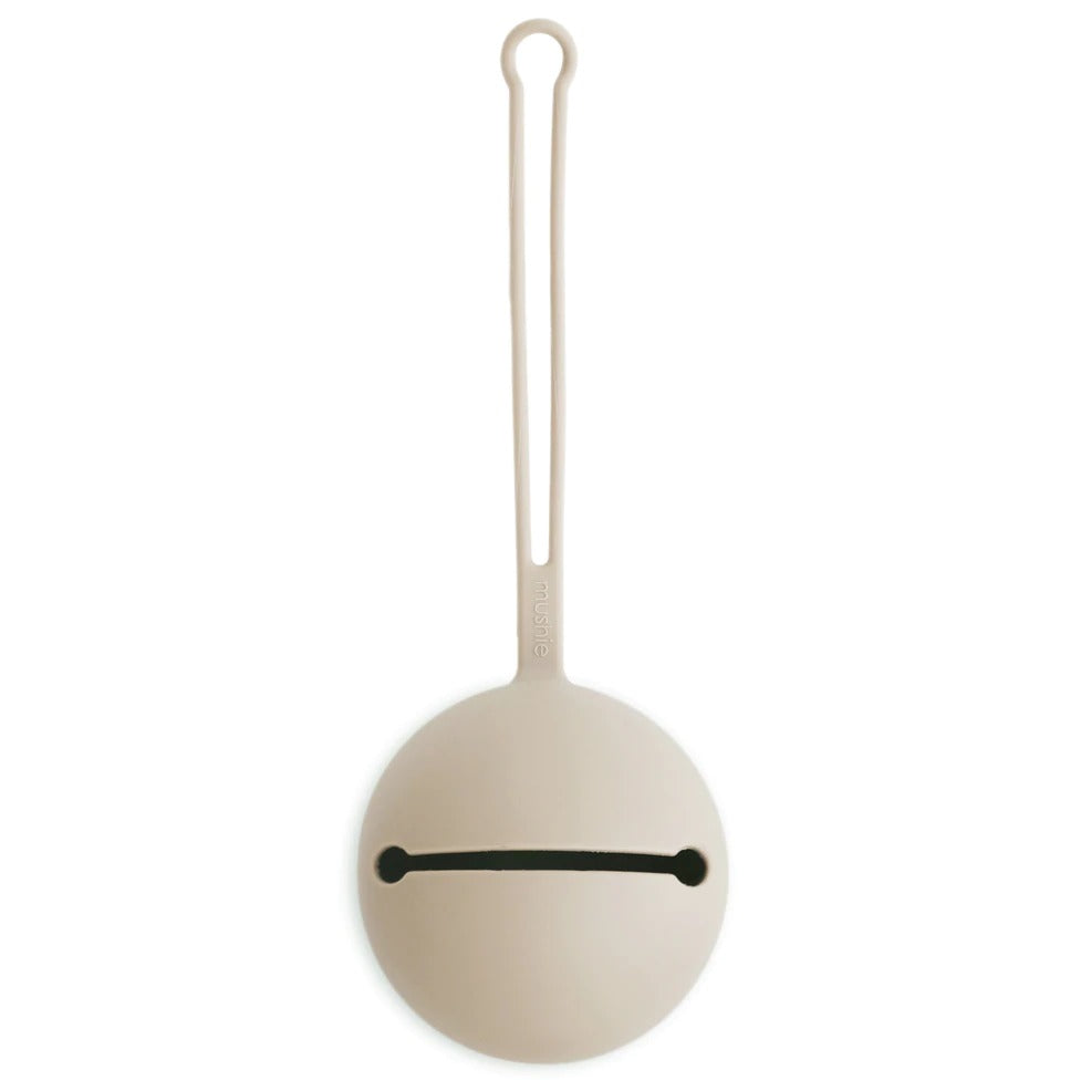 White background with a Silicone Pacifier Holder Case in Shifting Sand by Mushie. Case has a ball end with a slit through it, to put your pacifiers in, and a long strap to attach anywhere, in a beige colour.
