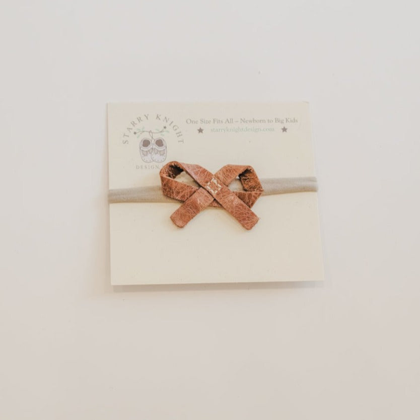 White background with the Ballet Bow Headband in Maple by Starry Knight Design. Headband is on a nylon band, with a simple leather tie bow, in a warm brown colour.