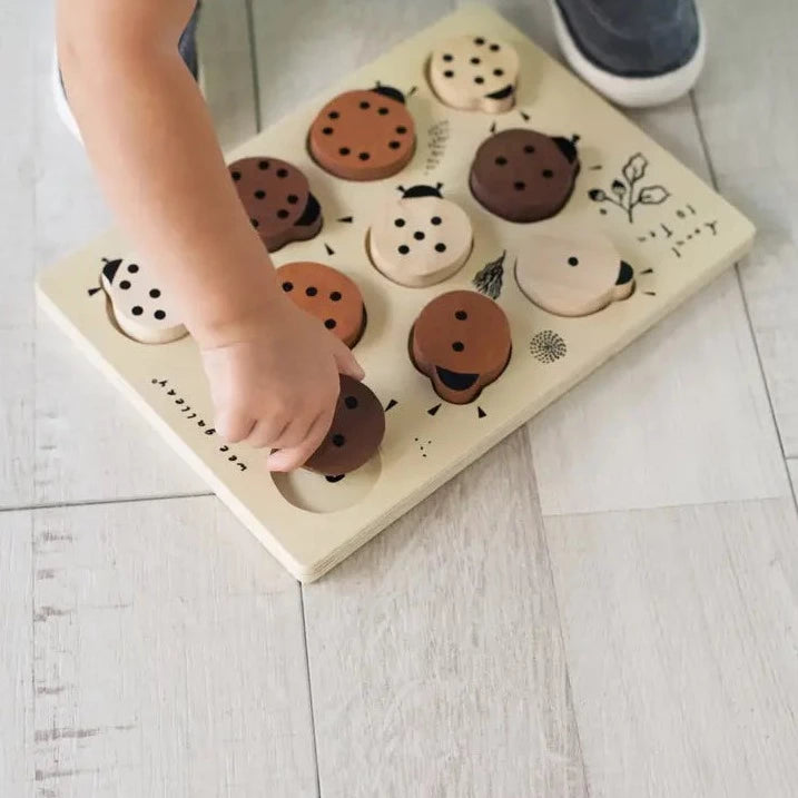 Model playing with wooden tray puzzle - count to 10 ladybugs by Wee Gallery, standing on a wooden floor. 