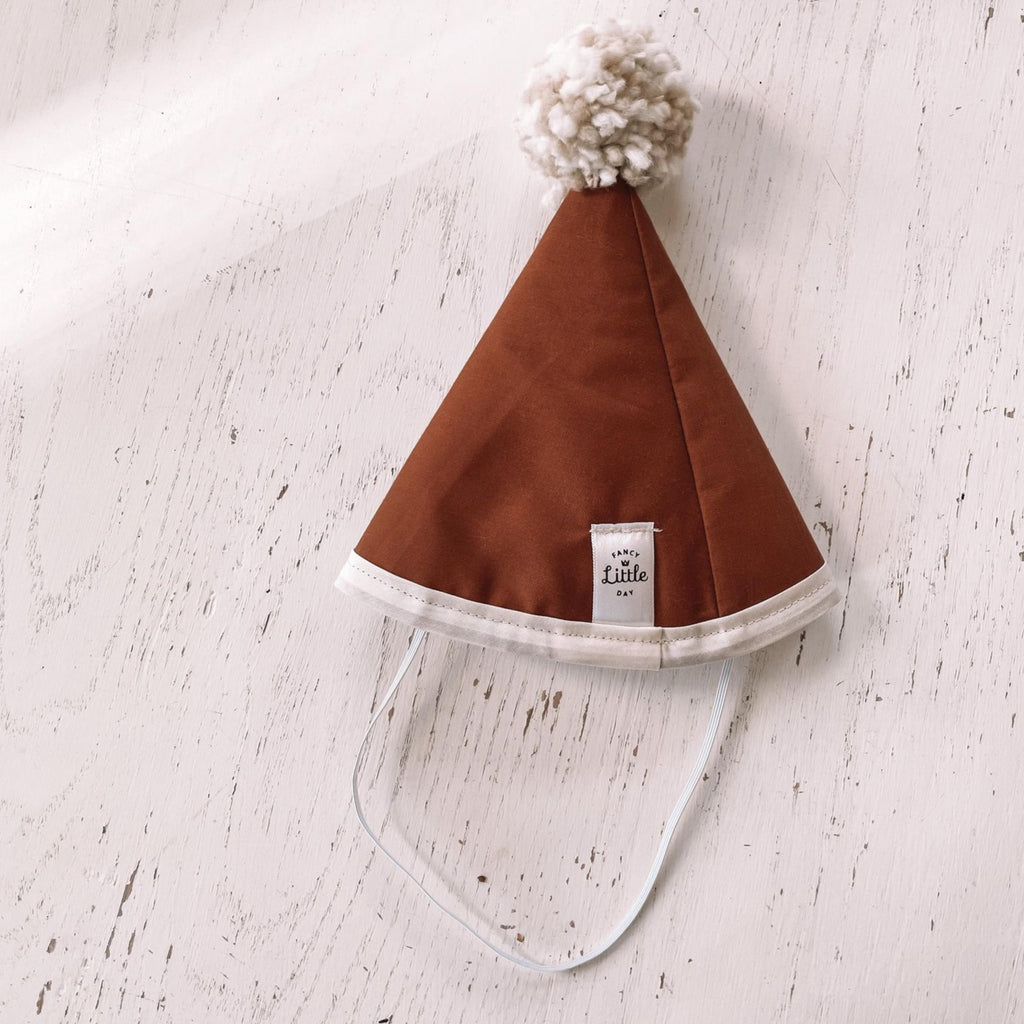 White washed wood background with Rust Fabric Party Hat and Beige Pompom by Fancy Little Day.