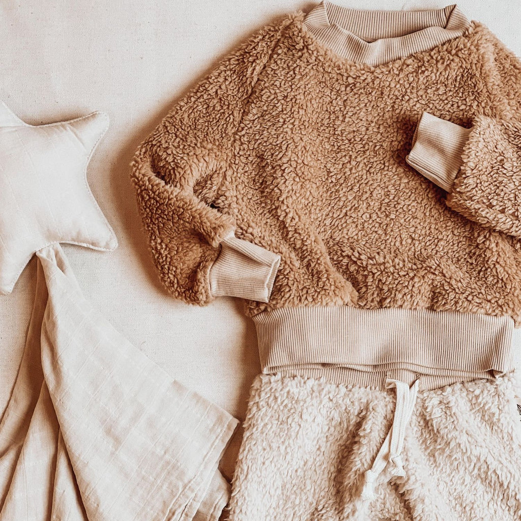 Teddy crew neck sherpa and Fawn pants by Petit Nordique, with a star teething blanket on a cream surface. 