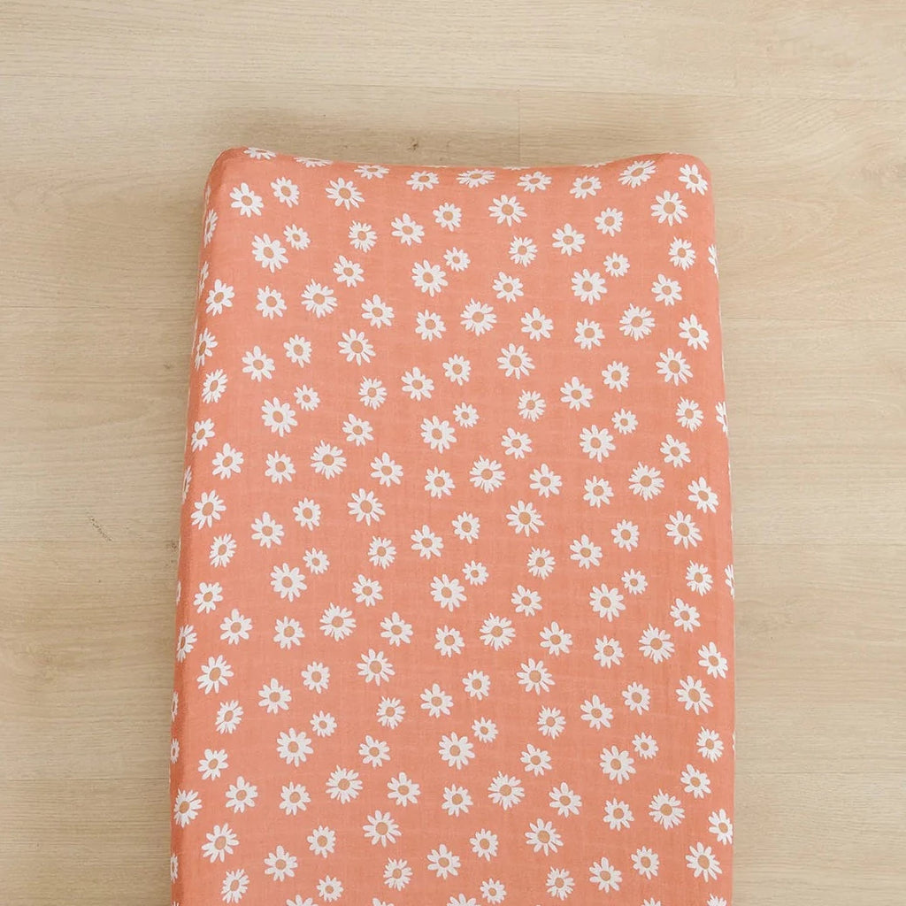 Light wood floor background with a changing pad with an Arizona Daisy Changing Pad Cover by Mebie Baby on it. Changing pad is orange with daisies all over, and fits snug.