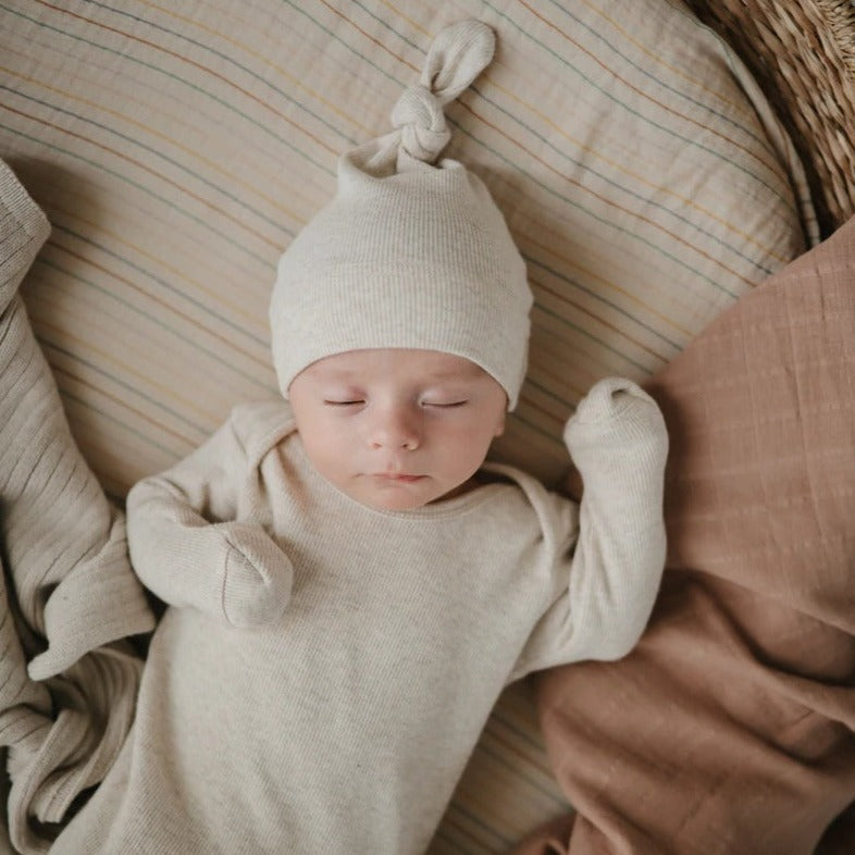 Overhead view of a baby sleeping in a bassinet, wearing a Ribbed Baby Beanie by Mushie.