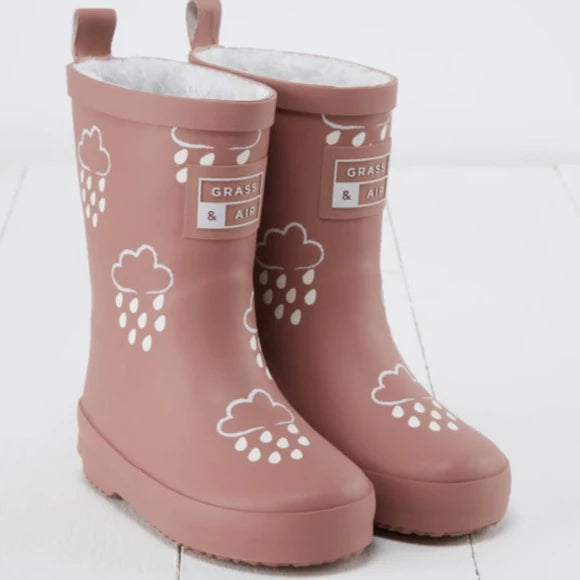 White background with Colour Changing Rain Boots in Rose by Grass & Air. Rainboots are a mauve colour, with white rain clouds all over, a fluffy interior, and a tag on the fron that says "Grass & Air".