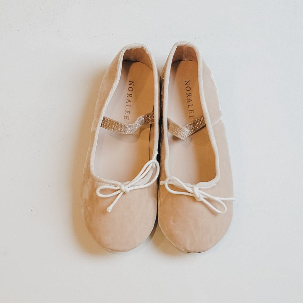 White background with Ballet Flats in Antique by Noralee. Ballet flats are a cream velour with a sparkley strap over the top and small tie bows on the front.