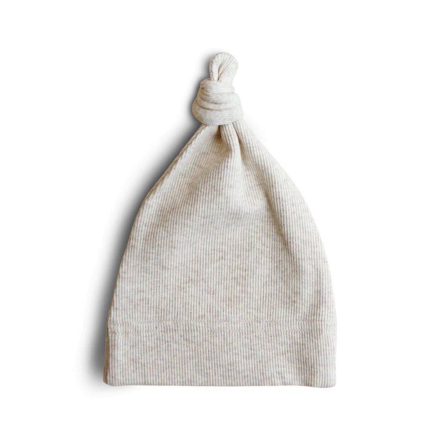 White background with the Ribbed Baby Beanie in Beige Melange by Mushie. Beanie is made of a ribbed oatmeal knit, and has a knot on the top.