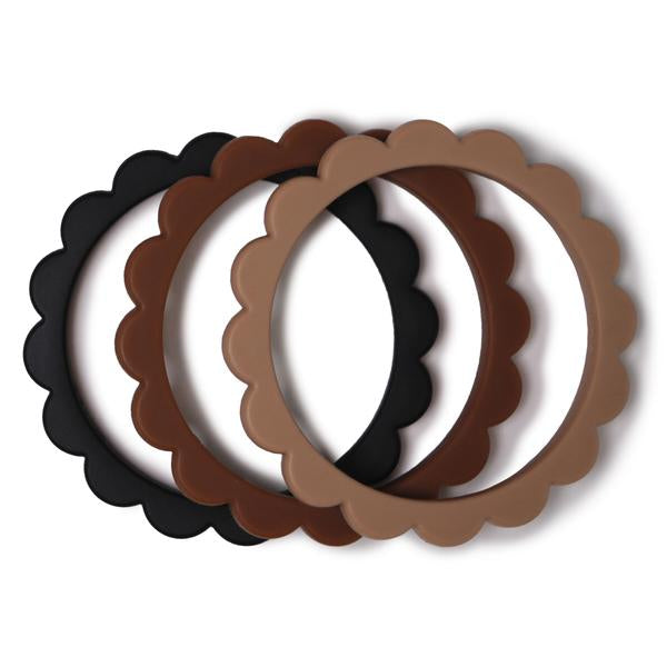 White background with Flower Teething Bracelet 3-Pack in Black/Natural/Caramel by Mushie. These are round bracelets, that look like flower petals - comes with a black, brown, and reddish brown bracelet.