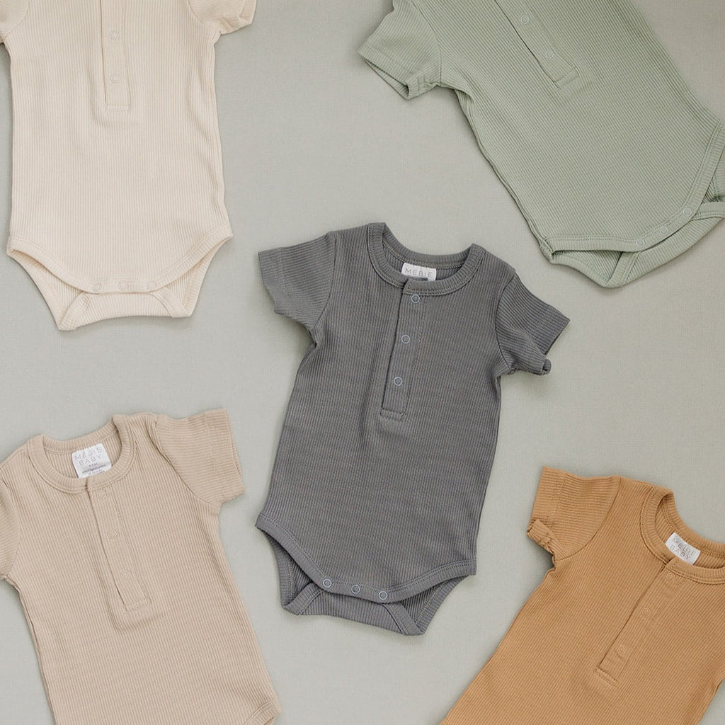 Mebie Baby bodysuits in multiple colours, laid on a beige surface. 