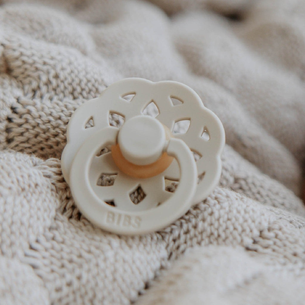 Close up of a Boheme Size 2 Pacifier in Ivory by Bibs in a cream blanket.