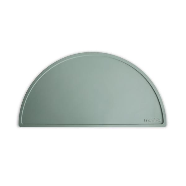 White background with Silicone Place Mat in Cambridge Blue by Mushie. Placemat is a blue/green colour, made of silicone, and in a semicircle.