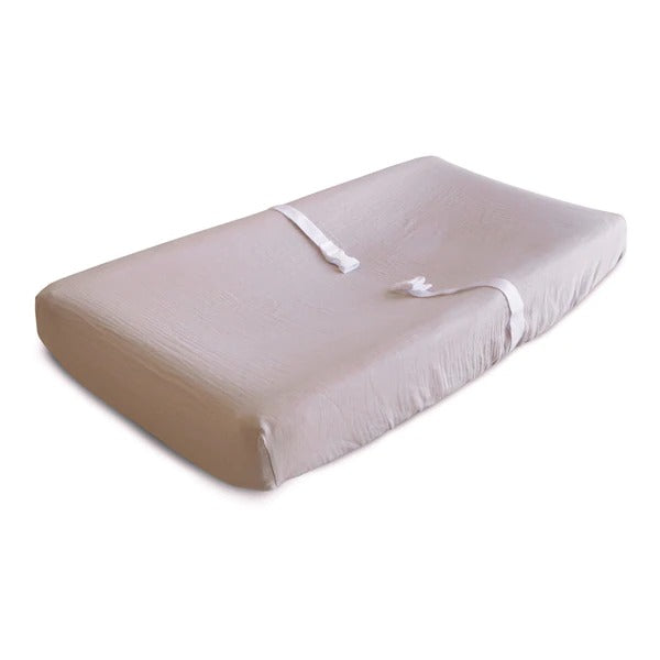 White background with a changing pad, and an Extra Soft Muslin Changing Pad Cover in Blush by Mushie on it. Blush is a neutral pink colour.
