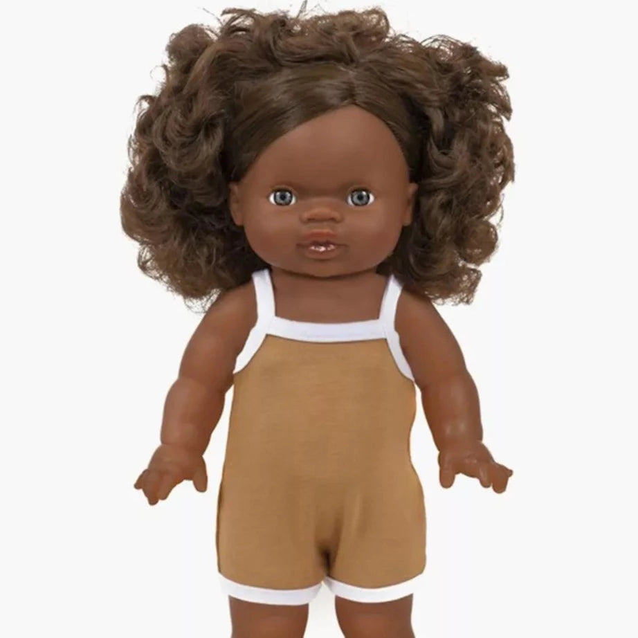 White background with Charline Doll by Minikane. Doll has black skin, and dark curly hair, with a spaghetti strap romper in an ochre colour.