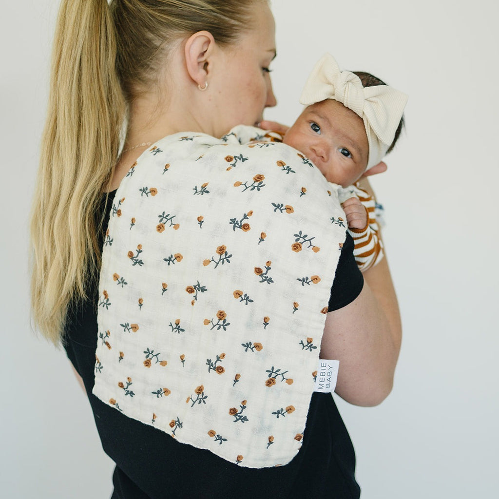Cream Floral Burp Cloth by Mebie Baby, with a mother holding her newborn baby over her shoulder. Standing in front of a white wall. 