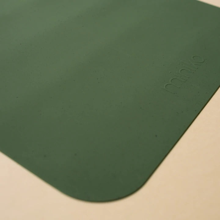 Beige background with a Silicone Placemat in Leaf by Minika. Placemat is square silicone, in an emerald green colour.