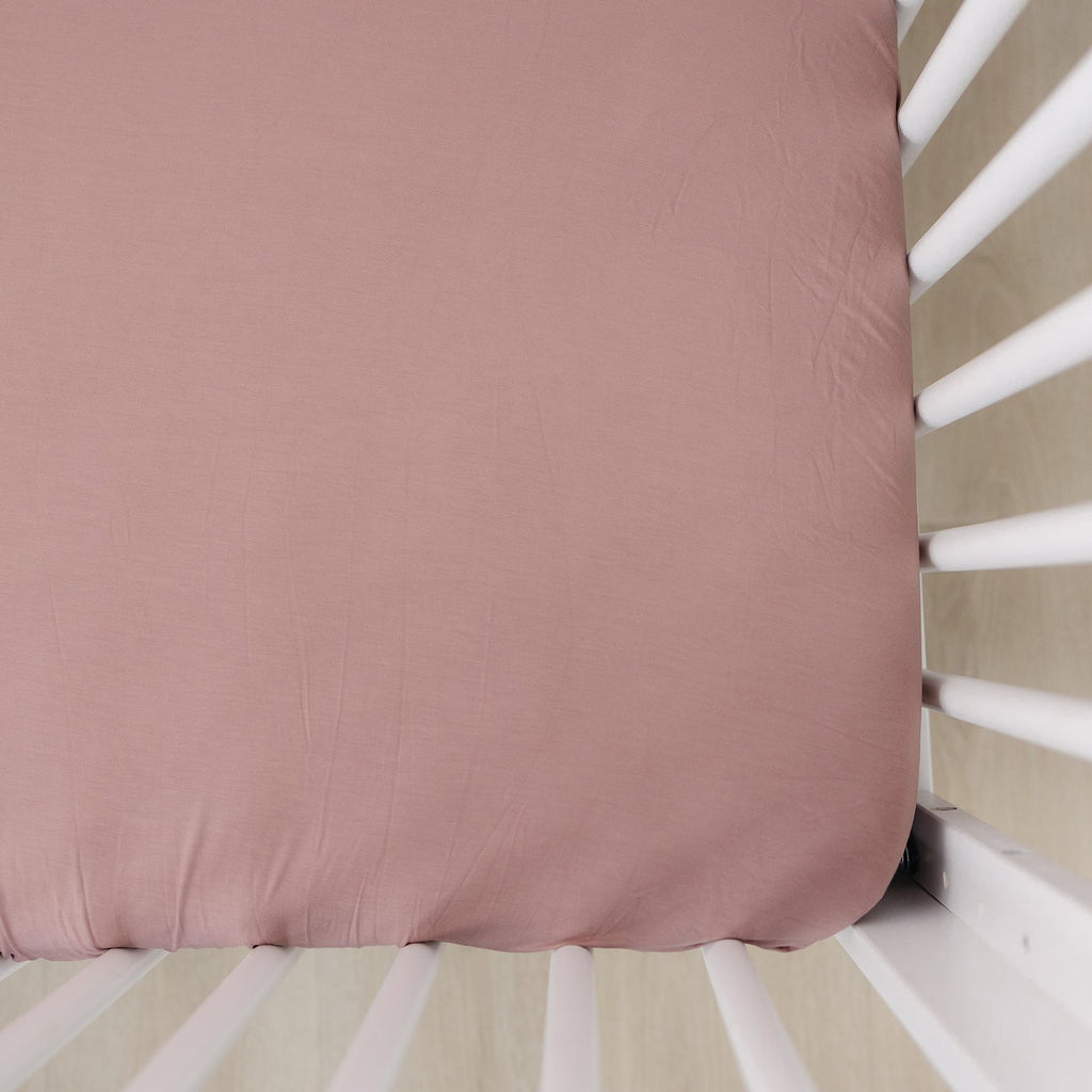 Overhead view of a Dusty Rose Stretch Crib Sheet by Mebie Baby on a mattress. Crib sheet is a dusty rose colour, and fits snug to mattress.