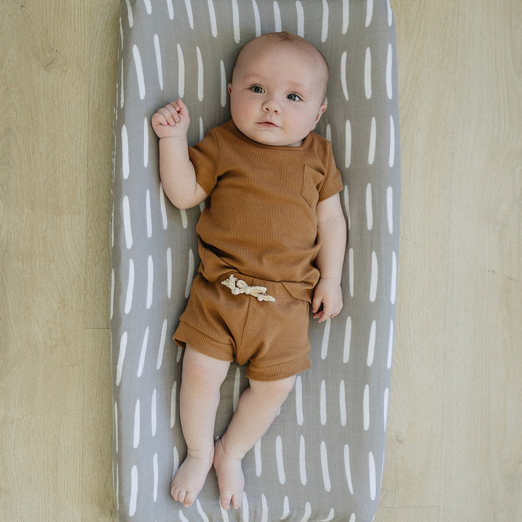 Baby on a Grey Dash Change Pad Cover by Mebie Baby on a wood floor. 