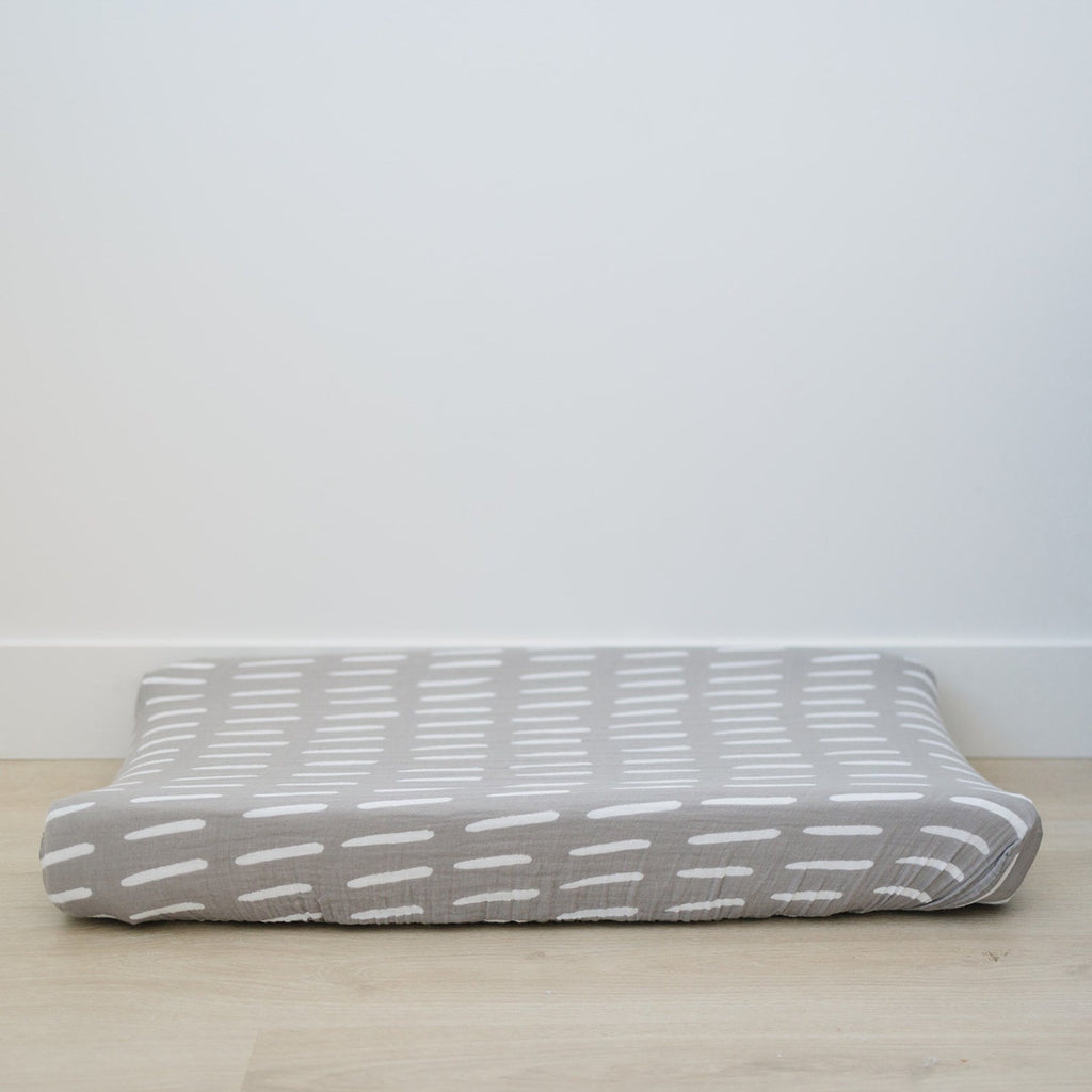 Grey Dash Pad Cover by Mebie Baby on a change pad, in front of a white wall on a wood floor. 
