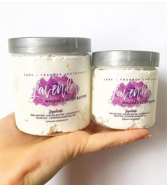 White background with hand holding 2 Whipped Body Butter by Jane + Thunder in Lavender. Showing both size options available.