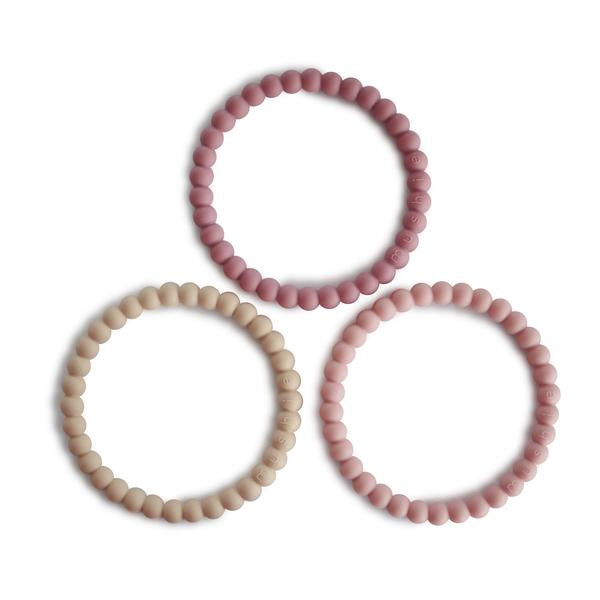 White background with Pearl Teething Bracelet 3-Pack in Linen/Peony/Pale Pink by Mushie. These are bracelets with a pearl style bead, in 3 different colours; a beige, rose, and blush colour.