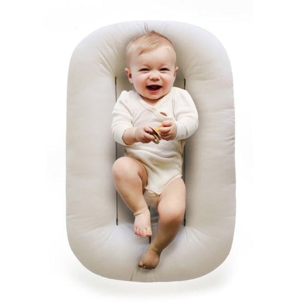 White background with an overhead view of a baby laying in the Snuggle Me Organic Infant Lounger in Natural by Snuggle Me. Lounger is a cream colour.