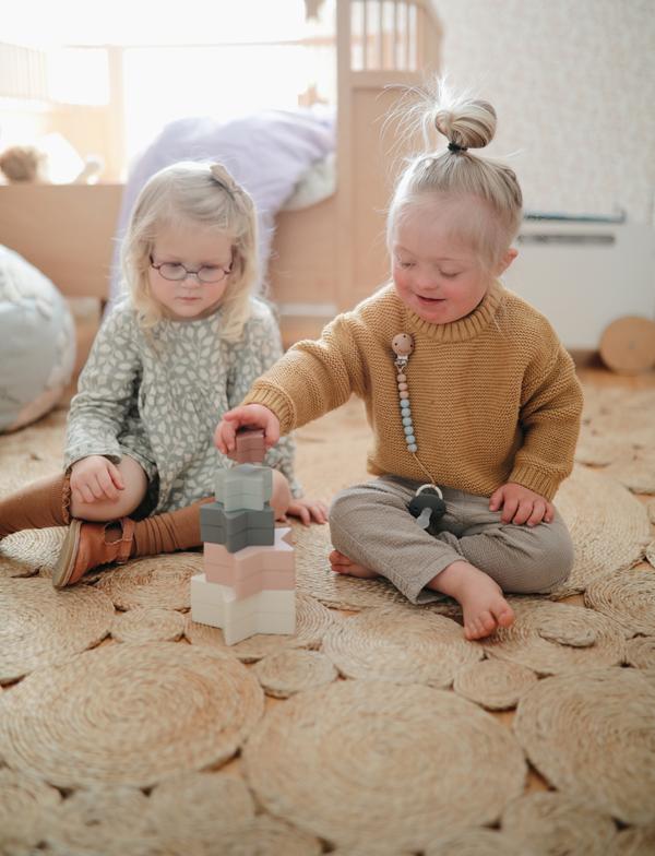 Two little girls sitting in a room, stacking the Nesting Stars Toy by Mushie.