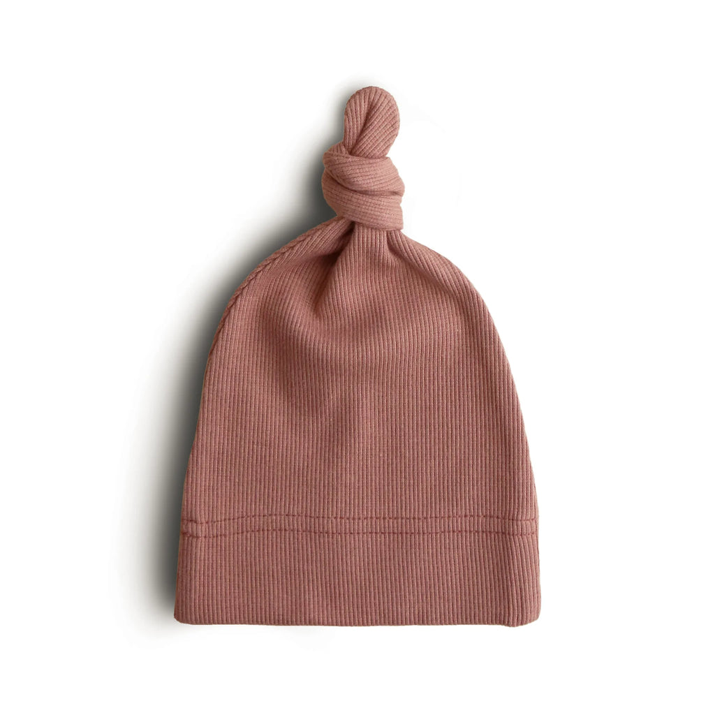 White background with Ribbed Baby Beanie in Cedar by Mushie. Beanie is a ribbed burgundy colour with a knot on the top.