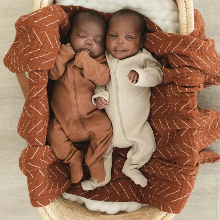 Overhead view of 2 babies laying in a bassinet, one is wearing the Rust Organic Cotton Ribbed Zipper One-Piece by Mebie Baby. 