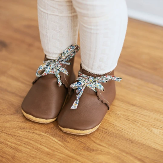Close up of a little girl wearing the Scalloped Boots in Espresso by Sun & Lace. Boots are a deep brown colour, with blue floral laces.