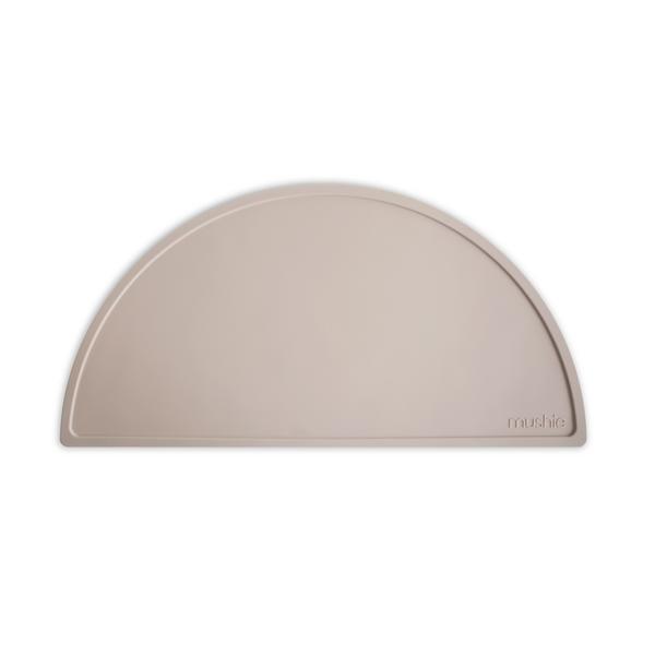 White background with Silicone Place Mat in Shifting Sand by Mushie. Placemat is beige, made of silicone, and in a semicircle.