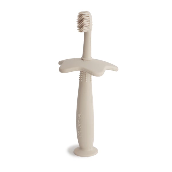 White background with Star Training Toothbrush in Shifting Sand by Mushie. Toothbrush is made out of silicone with a star shaped safety guard, and is a beige colour.