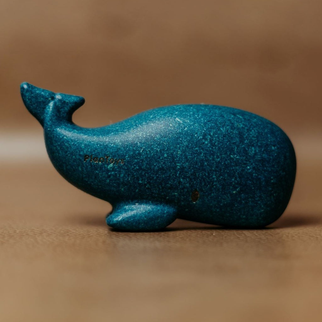 Brown background with Whale by PlanToys. Whale is blue, and made of wood.