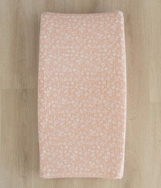 Overhead view of light wood floor with a Wildflower Changing Pad Cover by Mebie Baby on a change pad. Cover is a soft pink with white wildflowers all over.