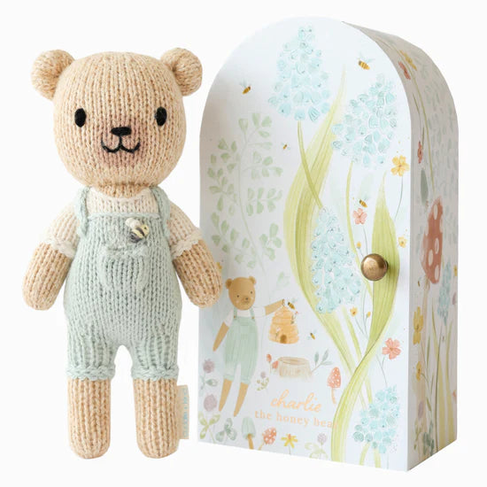 Brown bear with blue overalls standing beside floral box