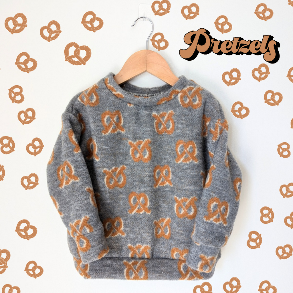 pretzel sweater on wood hanger with pretzels in the background 