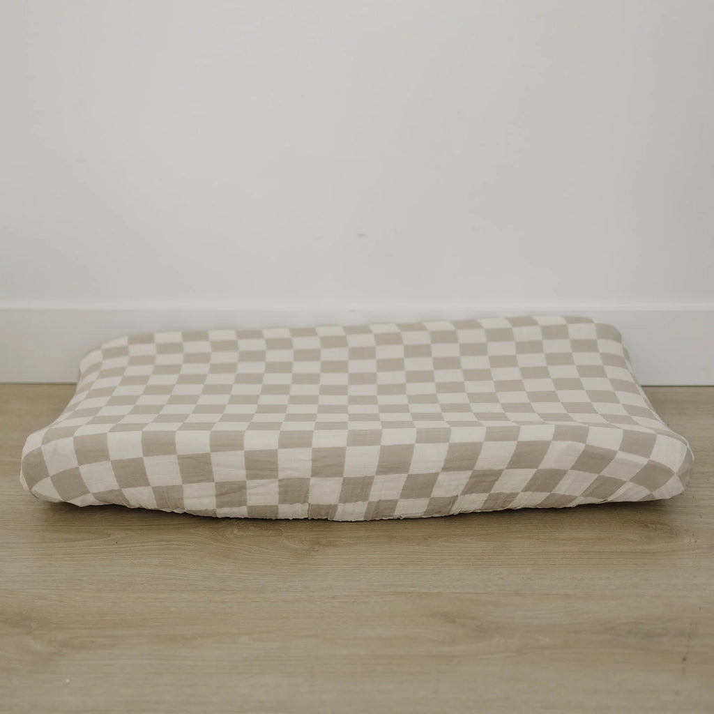 Taupe Checkered Changing Pad Cover by Mebie Baby on wooden floor against white wall
