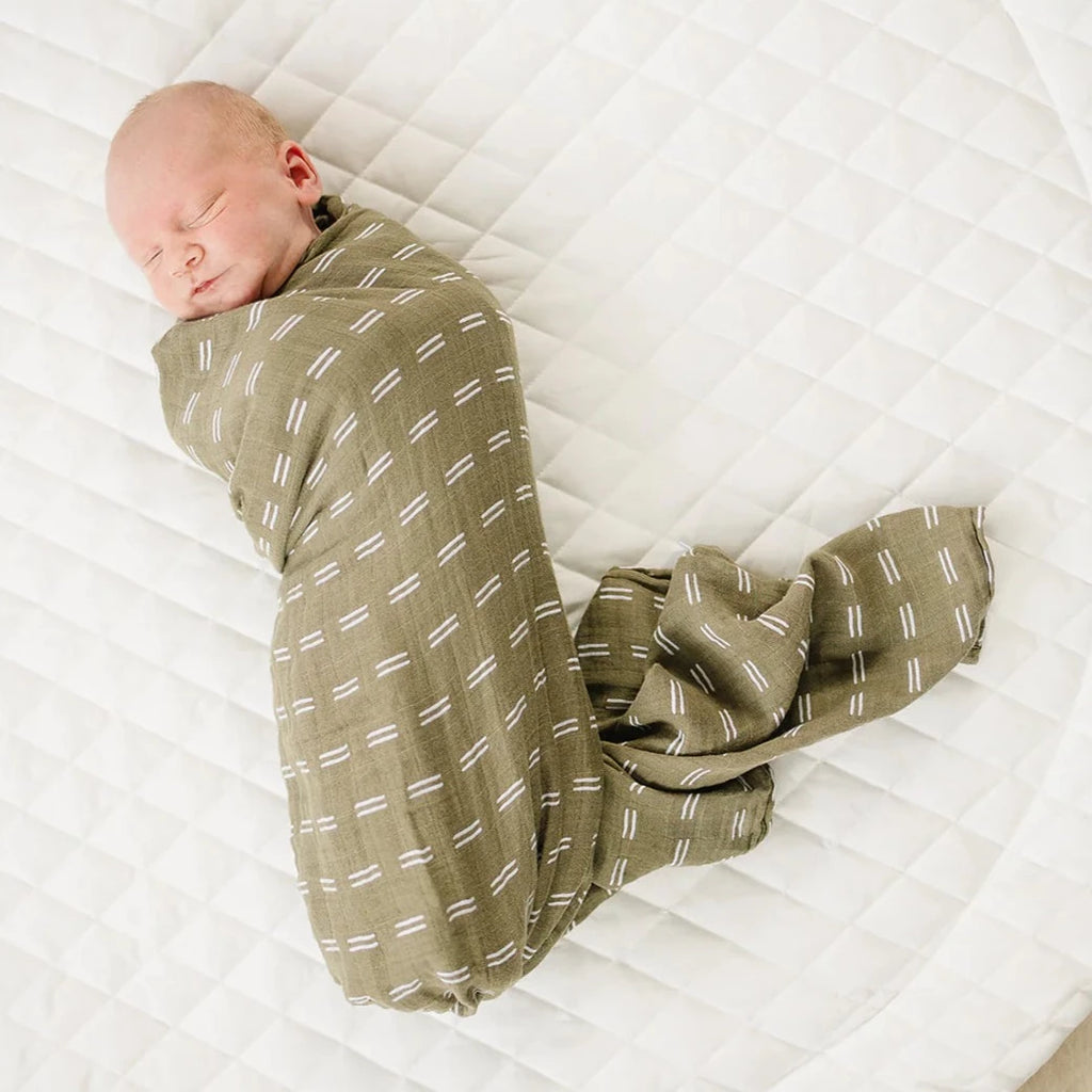 Olive Strokes Swaddle by Mebie Baby swaddle wrapped on sleeping baby on white quilted playmat