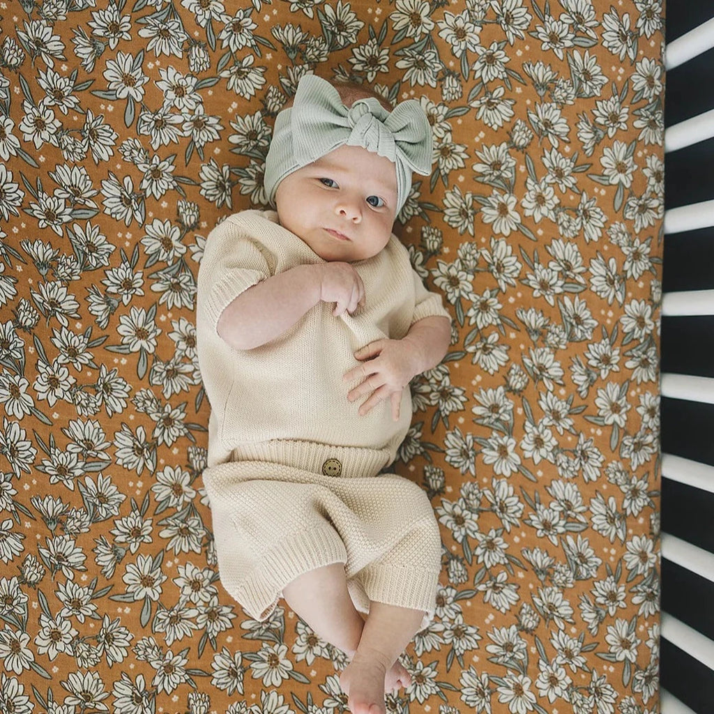 Magnolia Crib Sheet by Mebie Baby baby laying down on crib mattress with headband