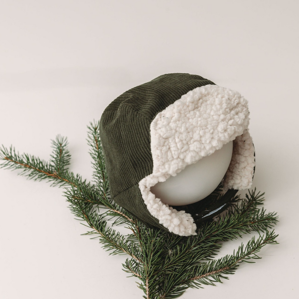 trapper hat on mannequin head with greenery and white background 