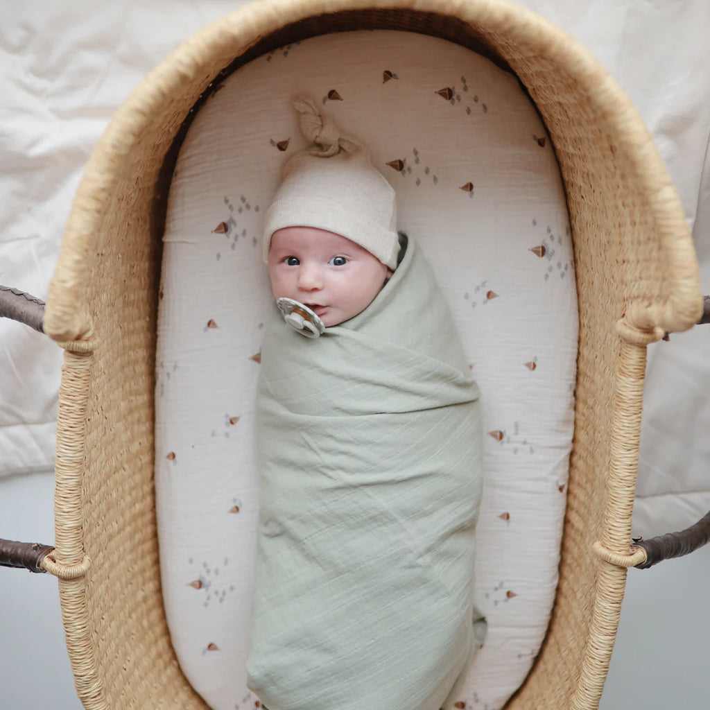 Muslin Bassinet Sheet | Boats by Mushie baby in wicker bassinet with white knot hat