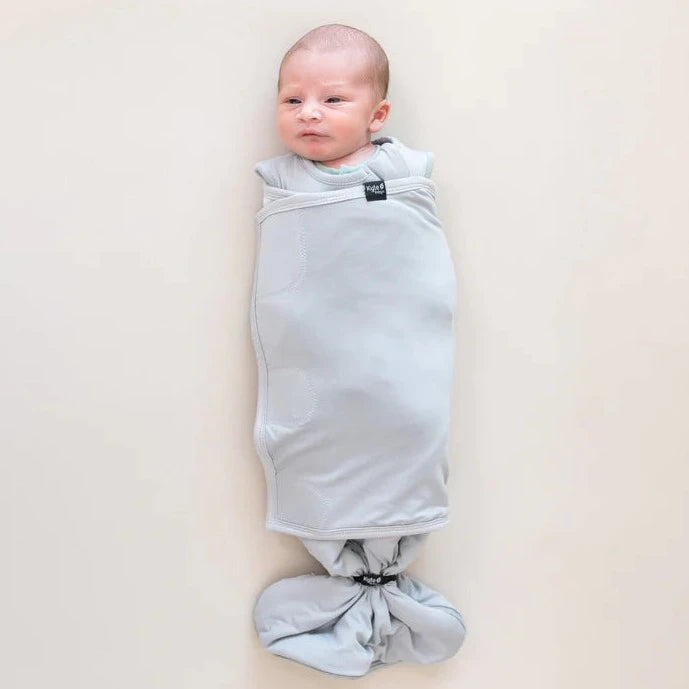 flatlay of baby wearing swaddle sac on white sheet 