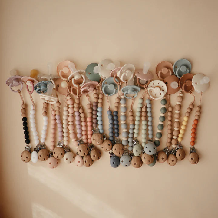 flatlay on brown background of pacififer clips with soothers on them 