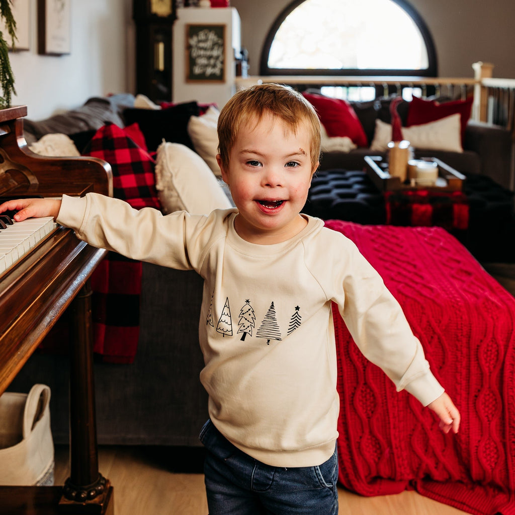 little boy with hand on piano in cream trees sweatshirt