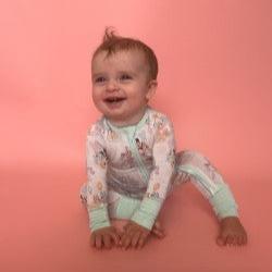 baby sitting with hands forward in character romper with pink background