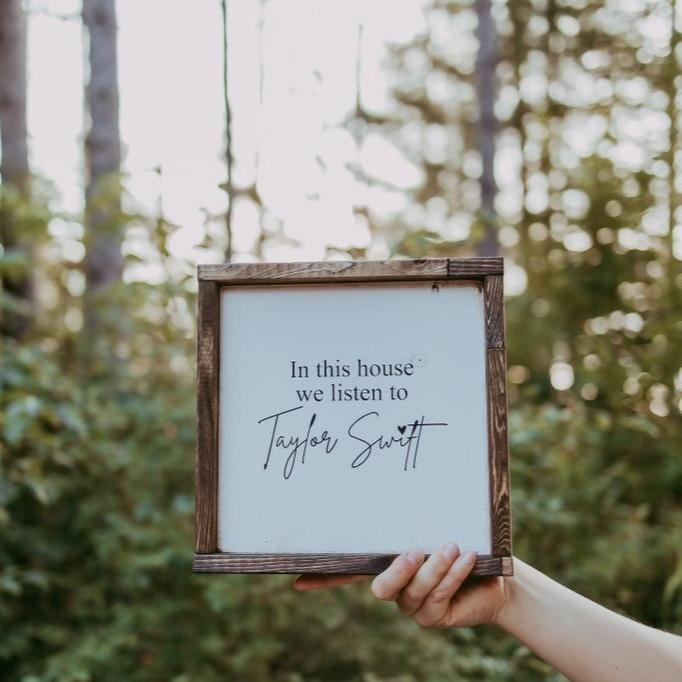 taylor switch in this house sign in hand with trees in background 