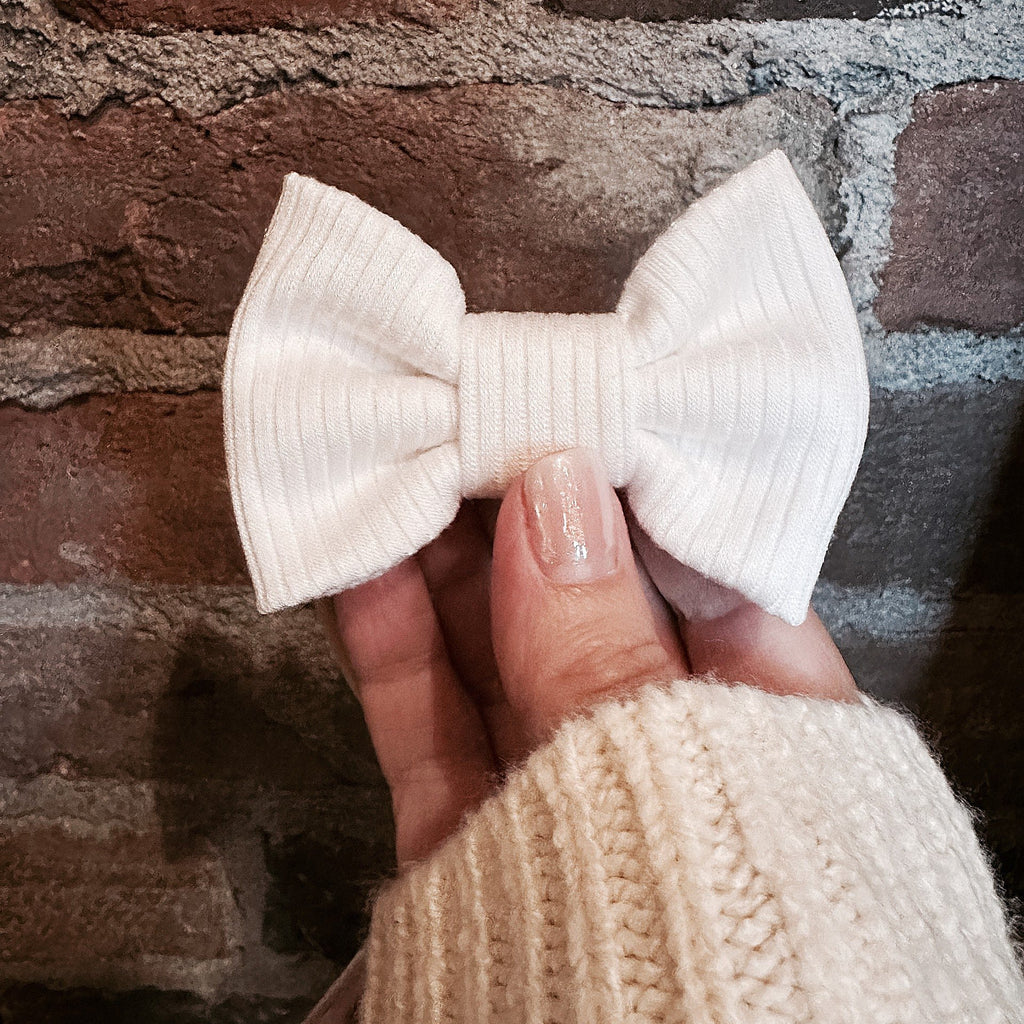 ivory mini bow in hand in front of brick wall