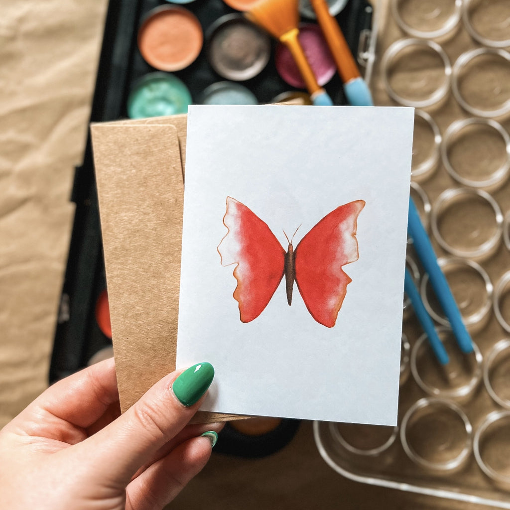 butterfly card in hand with paint colours in behind 