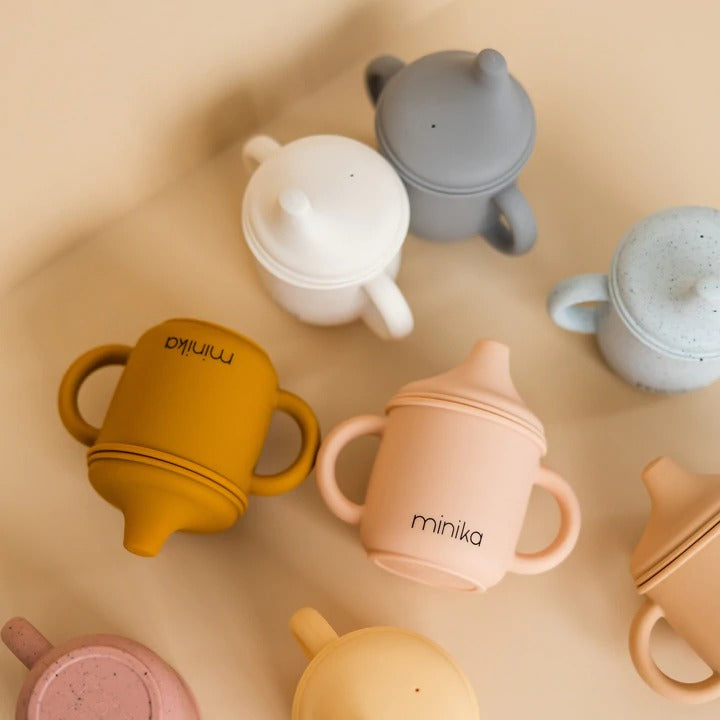 Beige background with overhead view of a pile of Silicone Sippy Cups by Minika.