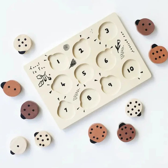 Wooden Tray Puzzle - Count to 10 Ladybugs by Wee Gallery. Lady bugs scattered on white surface with puzzle tray. 